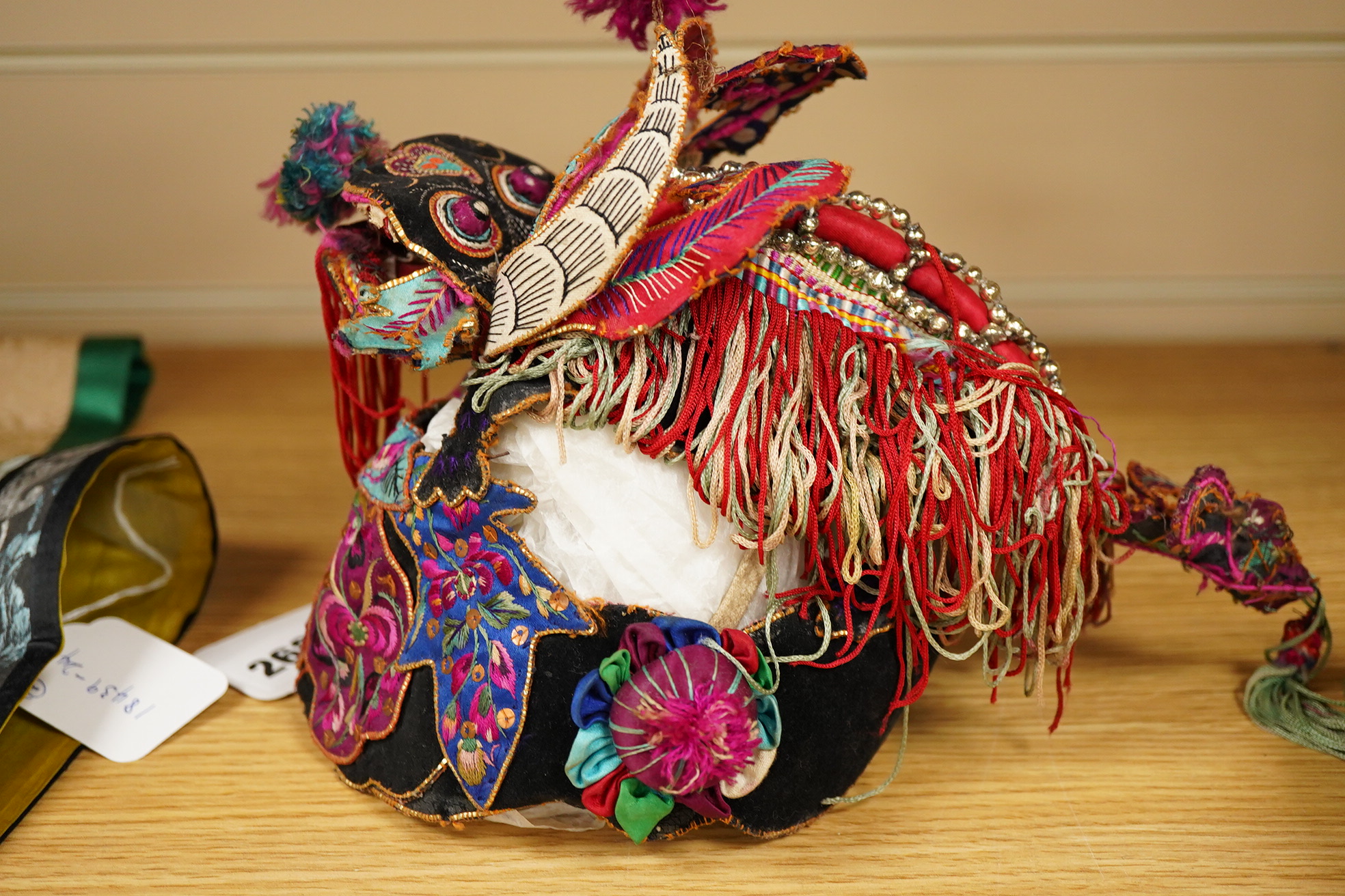 A decorative Chinese child’s festival ‘dragon’ hat, decorated with embroidered panels, tasselling and pom-poms with an elaborate dragon face and head dress. 20cm high. Condition - tasselling is missing around the dragons